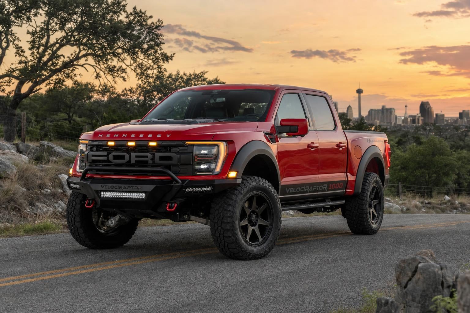 Red Hennessey VelociRaptoR 1000 Ford F-150 Raptor R on a Hill Country road with the San Antonio skyline and Tower of the Americas at sunset
